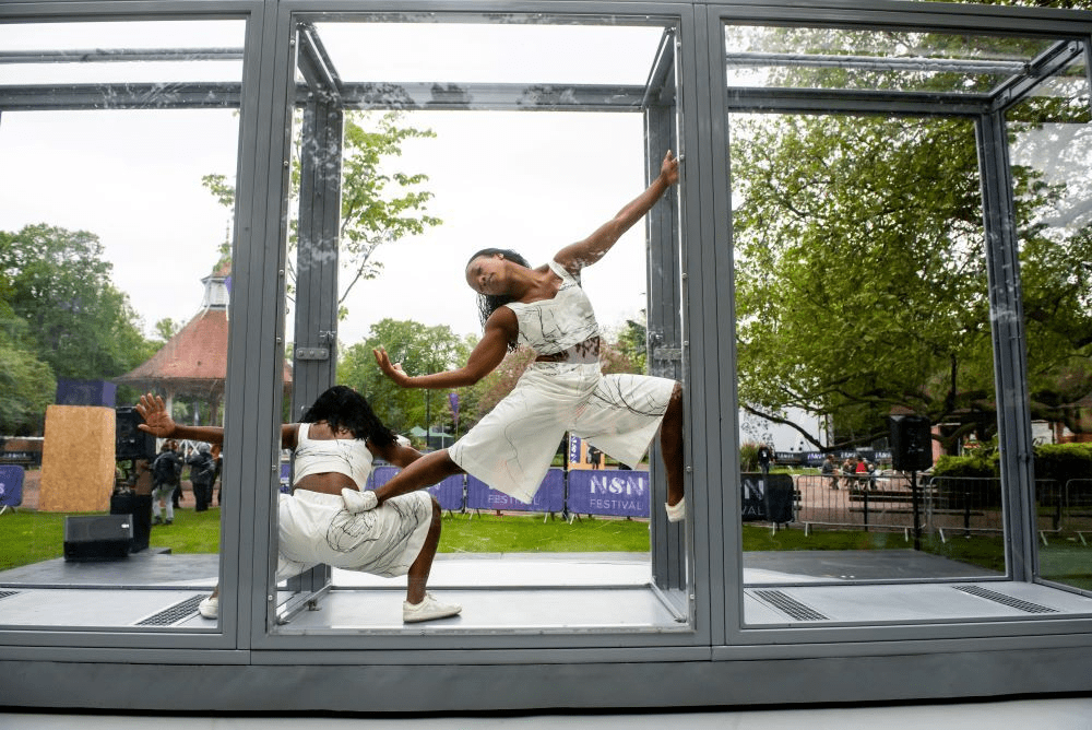 two dancers doing acrobatics inside perspex glass box