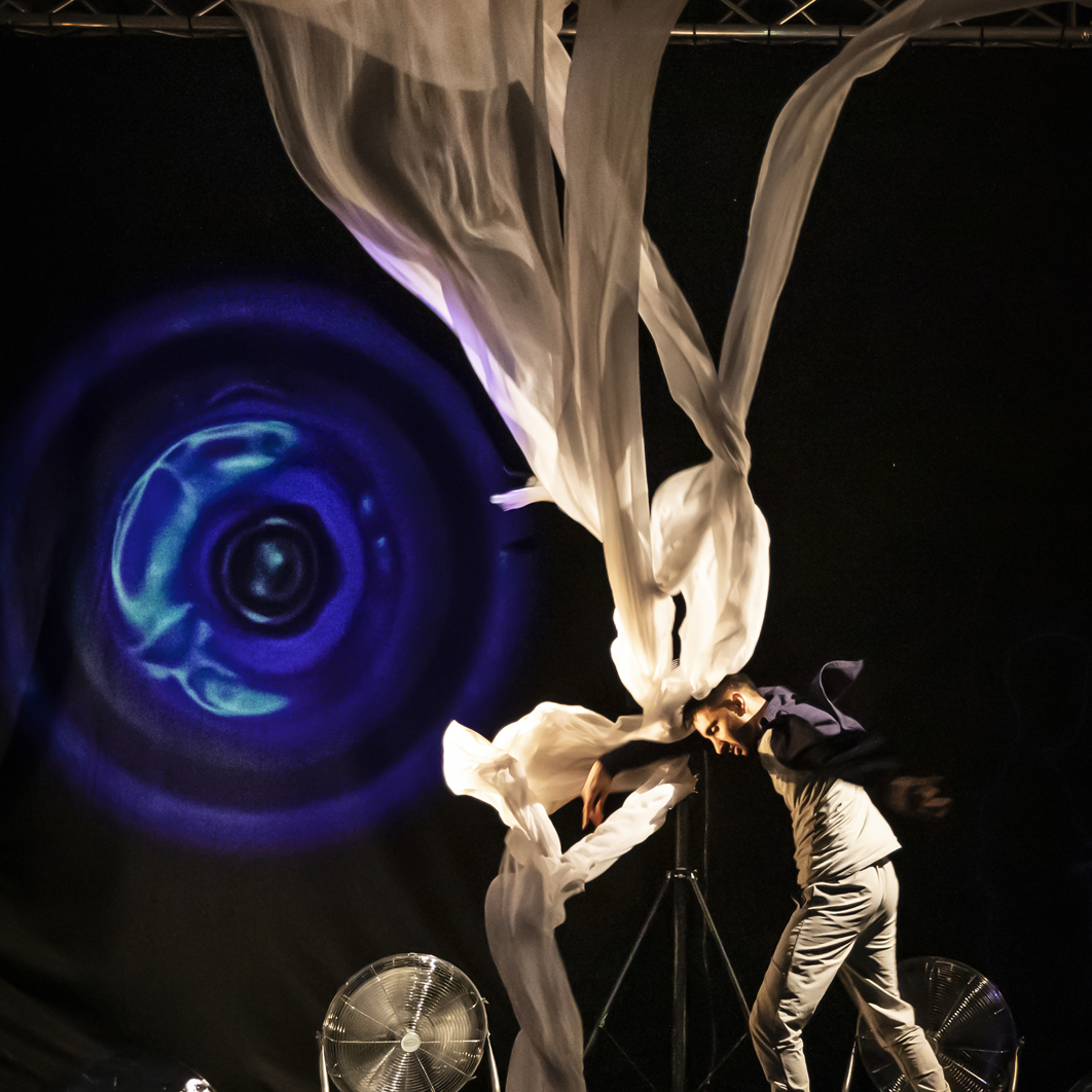 Aakash Odedra trying to make headway against a large sheet blown upwards by a fan