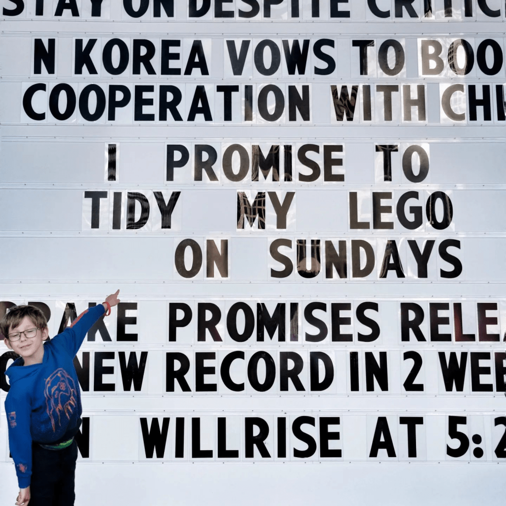 A smiling child proudly points at the giant promise board, which reads 'I promise to tidy my Lego on Sundays'